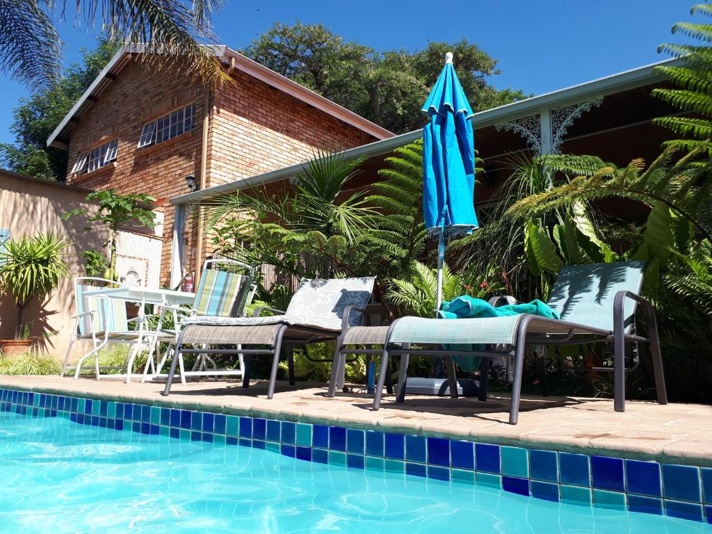 a pool with chairs and an umbrella next to a house at Vivian's Cottage in Pretoria