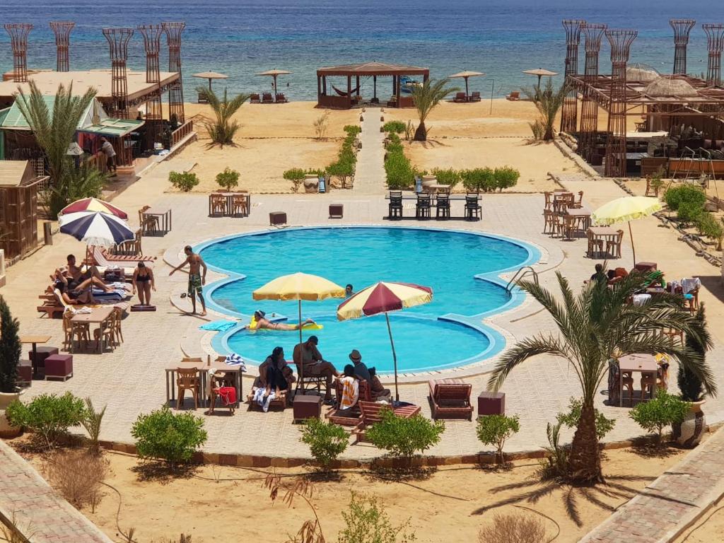 a swimming pool with people sitting around it next to the beach at Ciao Hotel in Nuweiba