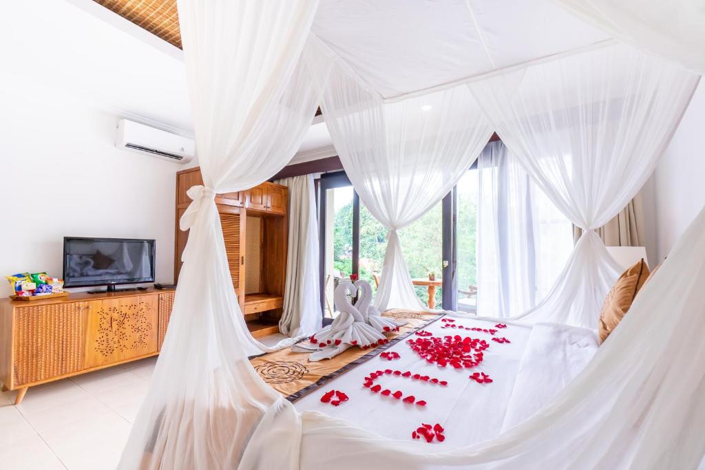 ein Schlafzimmer mit einem weißen Himmelbett mit roten Blumen darauf in der Unterkunft Villa Sonia Bisma in Ubud