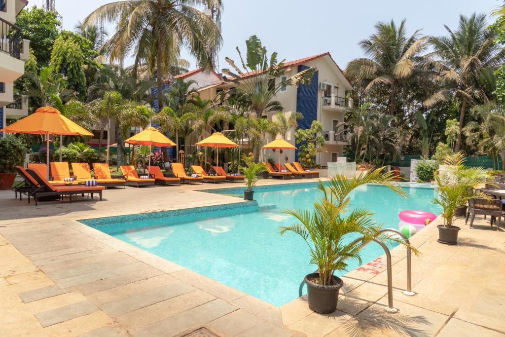 una piscina en un hotel con sillas y sombrillas en Kyriad Prestige Calangute Goa by OTHPL en Calangute