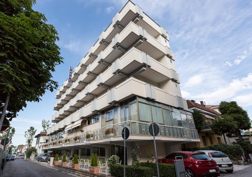wysoki biały budynek z samochodami zaparkowanymi przed nim w obiekcie Hotel Tre Assi w Rimini