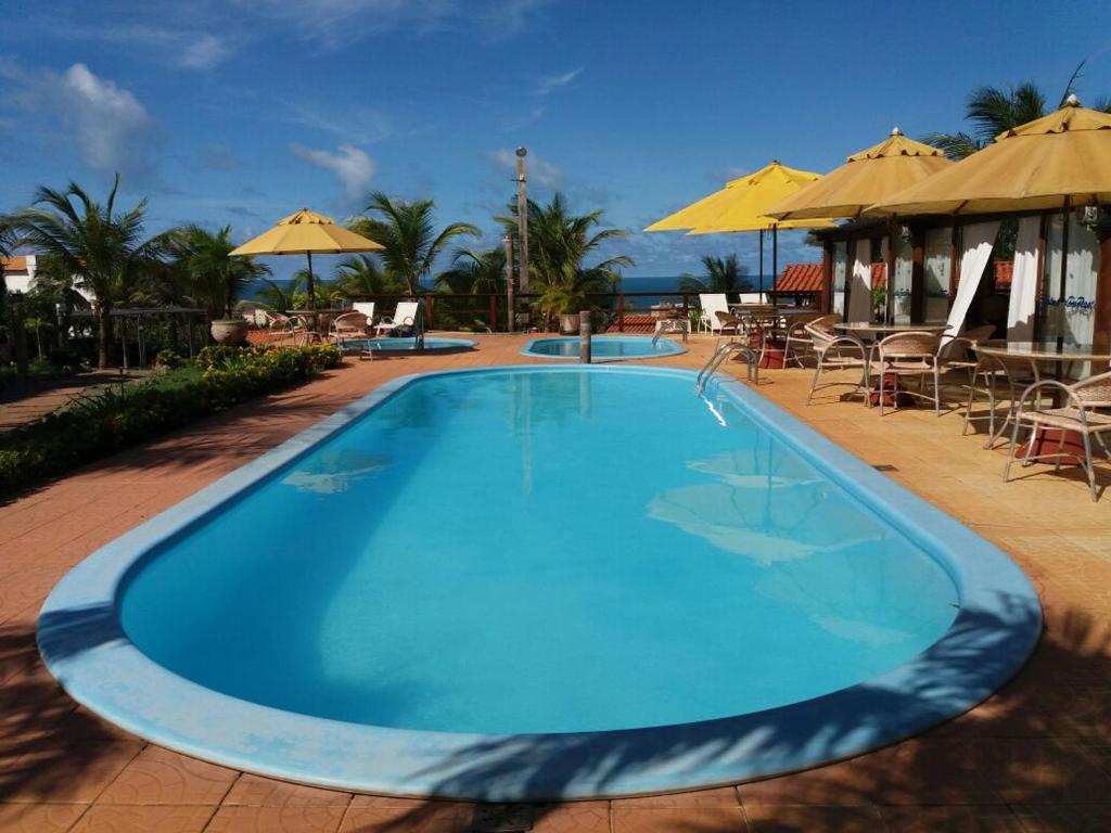 a large blue swimming pool with tables and umbrellas at Pousada Cultural Canto dos Poetas in Aquiraz