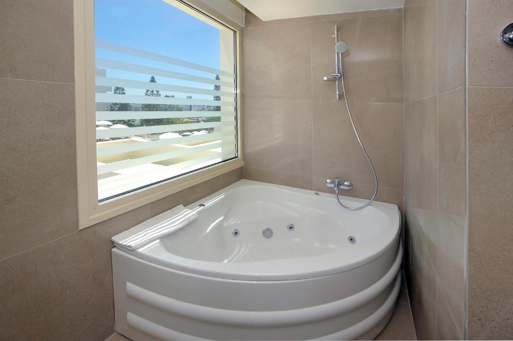 a white bath tub in a bathroom with a window at Nelia Beach Hotel & Spa in Ayia Napa
