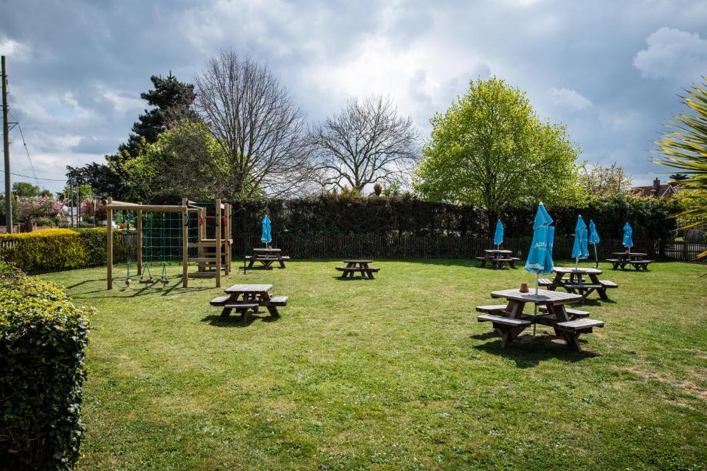 a park with picnic tables and a playground with blue umbrellas at The Randolph Hotel in Southwold