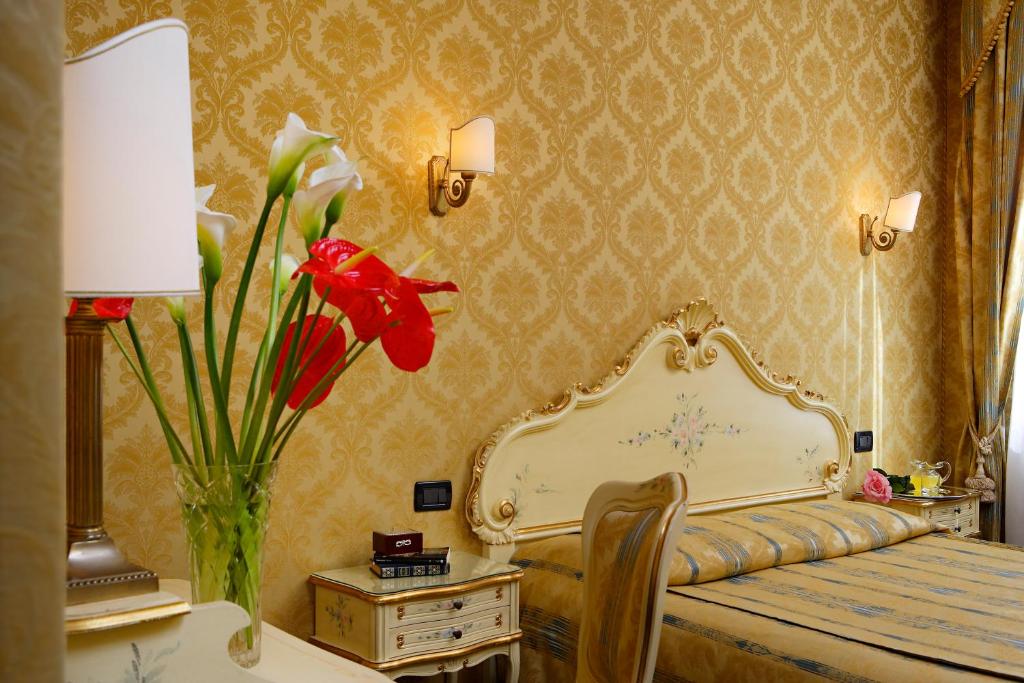 una camera con letto e vaso con fiori rossi di Hotel Gorizia a La Valigia a Venezia