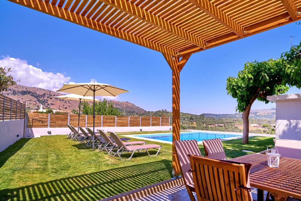 a patio with chairs and an umbrella and a pool at Villa Aelia in Georgioupolis