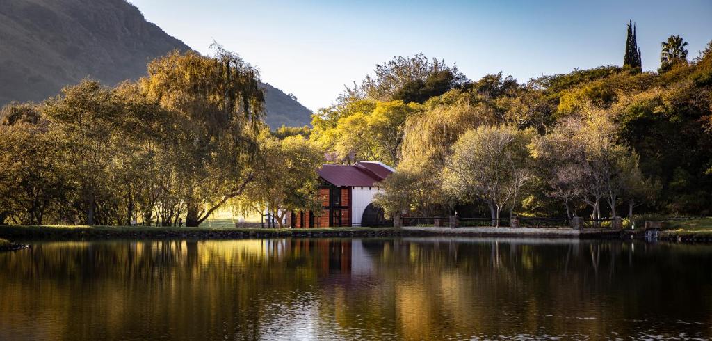 a building next to a lake with trees and mountains at Valley Of The Rainbow Estate in Dullstroom