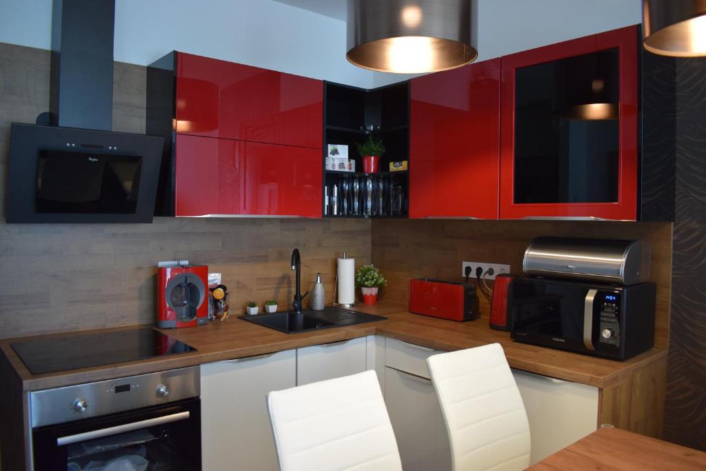 La cuisine est équipée de placards rouges, d'un évier et d'un four micro-ondes. dans l'établissement Lido Riviéra, Relux Apartman Balatonlelle, à Balatonlelle