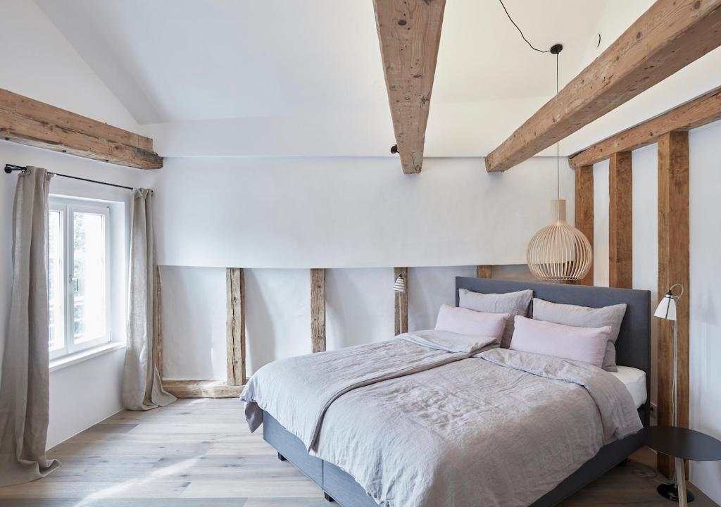 een slaapkamer met een groot bed met witte muren en houten balken bij Faktorei in Innsbruck