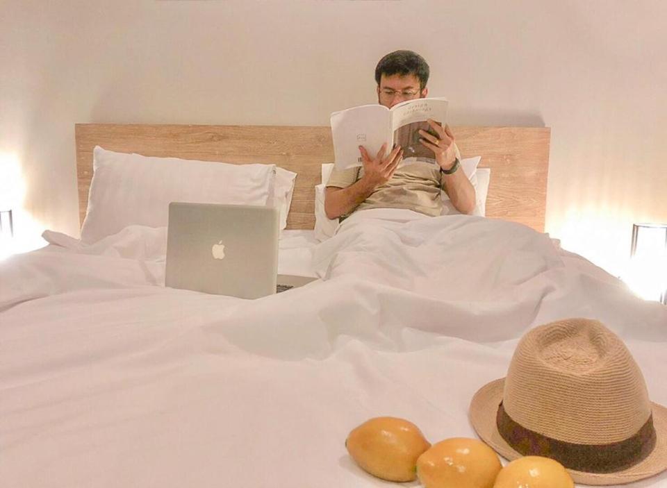 a man laying in bed reading a book with a laptop at Lemonade Phuket Hotel -SHA Plus in Chalong