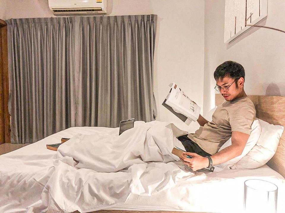 a man sitting on a bed reading a book at Lemonade Phuket Hotel -SHA Plus in Chalong