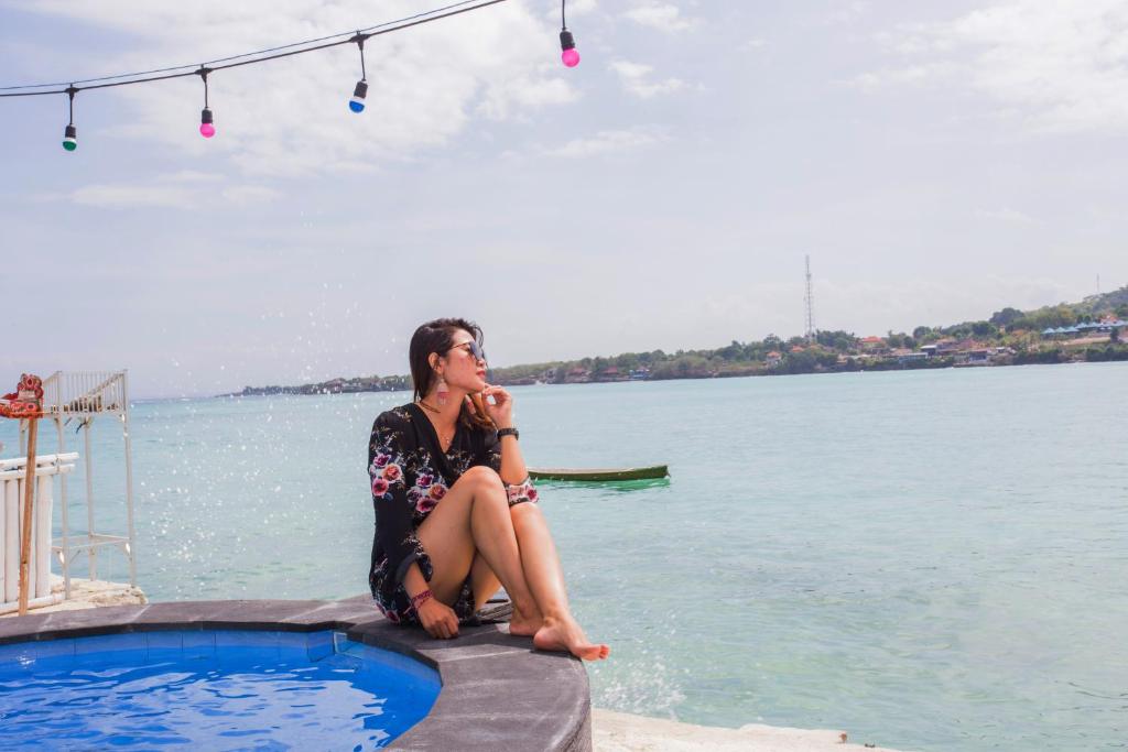 Eine Frau, die am Rande eines Pools neben dem Wasser sitzt. in der Unterkunft The Waterfront Beach House in Nusa Lembongan