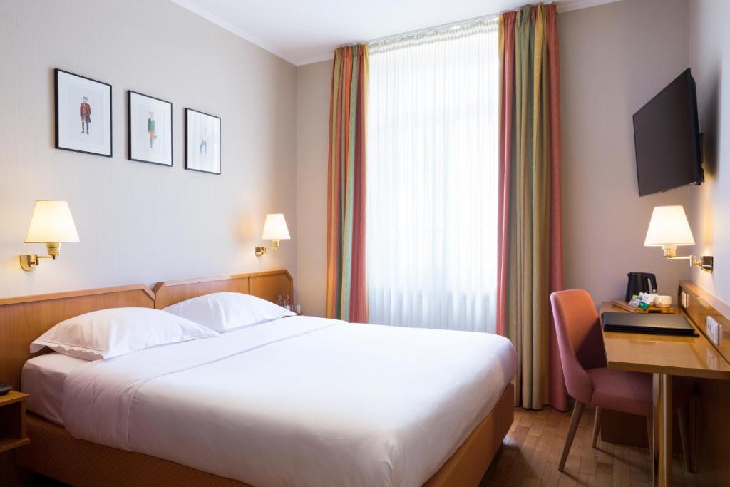 a hotel room with a large white bed and a desk at Hotel Perrin - former Carlton in Luxembourg