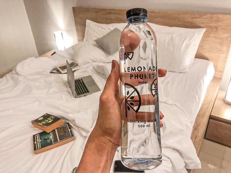 a person holding a bottle of water on a bed at Lemonade Phuket Hotel -SHA Plus in Chalong