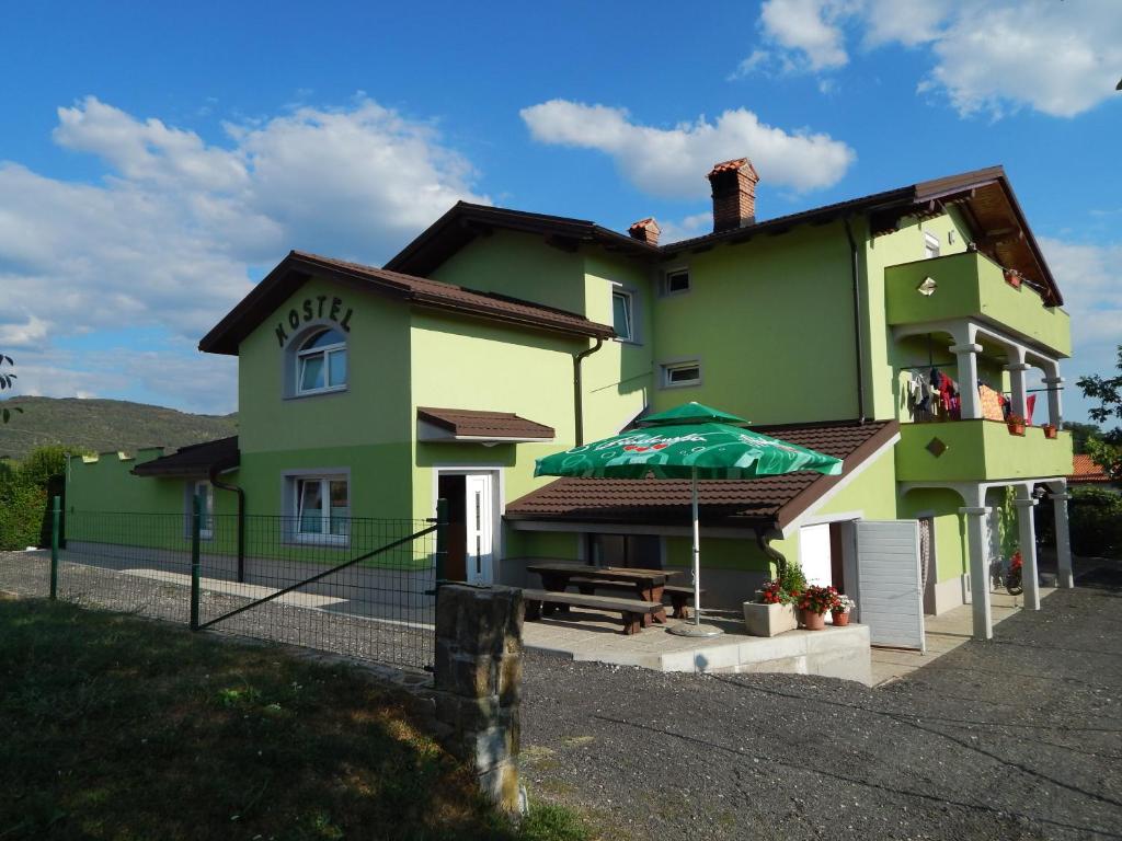una casa verde con mesa y sombrilla en Hostel Ociski Raj en Kozina