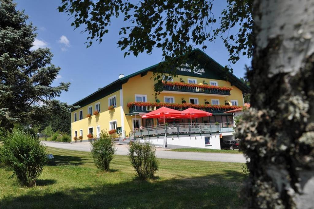 un edificio amarillo con sombrillas rojas delante en Café-Pension Kristall, en Harbach