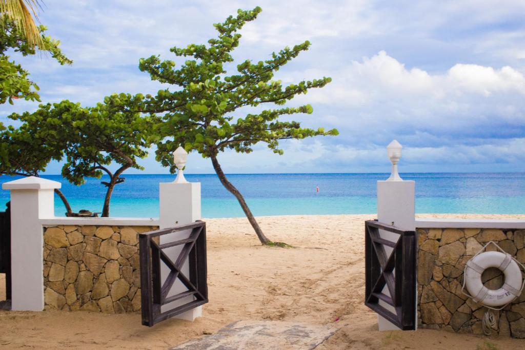 a gate on a beach with a tree and the ocean at Coyaba Beach Resort in Saint Georgeʼs