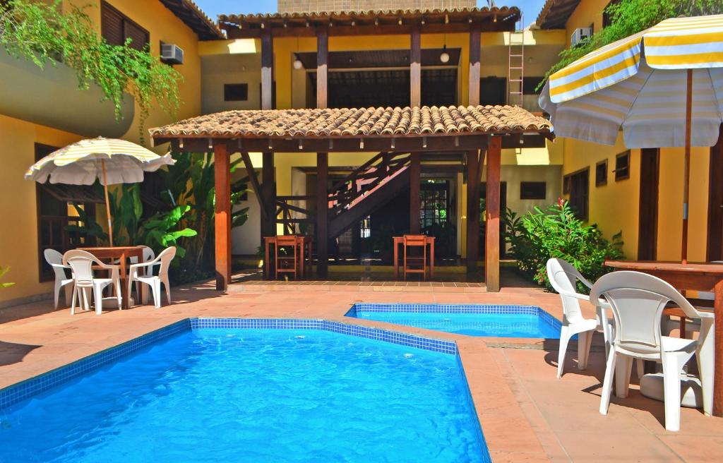 a swimming pool with chairs and a table and an umbrella at Pousada Clara in Cumuruxatiba