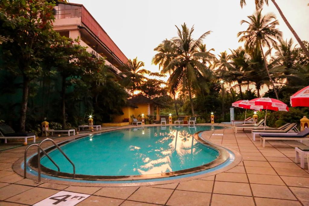 einen Pool in einem Resort mit Palmen und Sonnenschirmen in der Unterkunft Carina Beach Resort - 10mins walk to Benaulim Beach in Benaulim