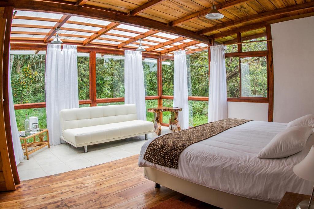 a bedroom with a bed and a couch and windows at San Isidro Lodge in Cosanga