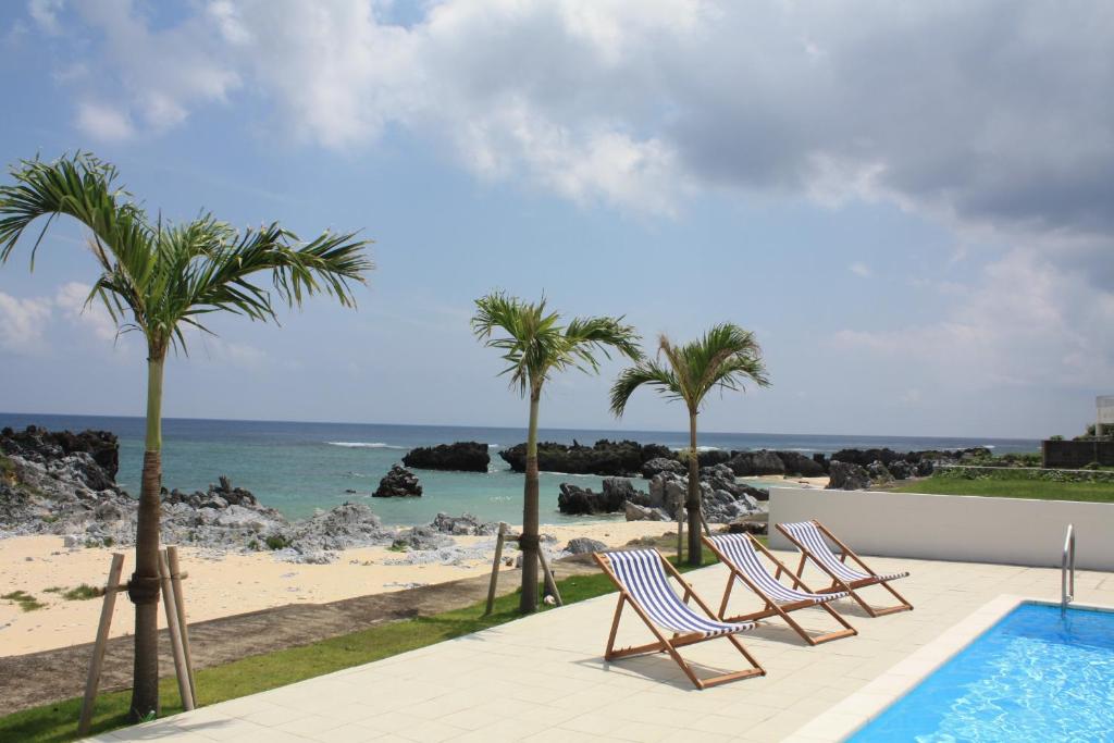 two chairs and palm trees next to a swimming pool at Thalassa Beach and Pool Villa in Yoron