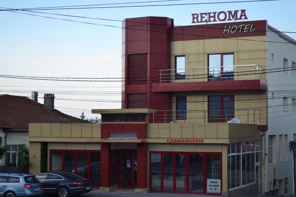 a red and yellow building with cars parked in front of it at Hotel Rehoma in Piteşti