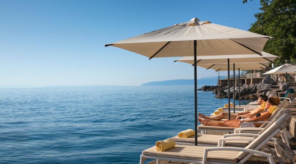 eine Gruppe von Menschen, die auf Liegestühlen neben dem Wasser sitzen in der Unterkunft Hotel Excelsior - Liburnia in Lovran