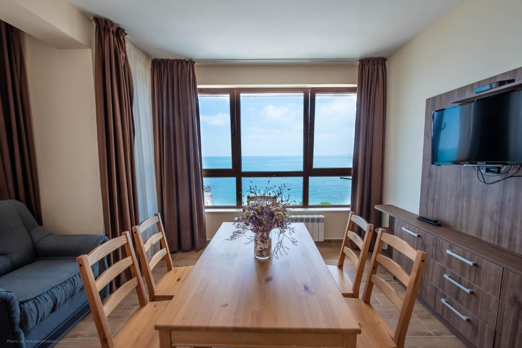 een woonkamer met een houten tafel met stoelen en een televisie bij Balchik Sea View Apartments in Princess Residence in Balchik