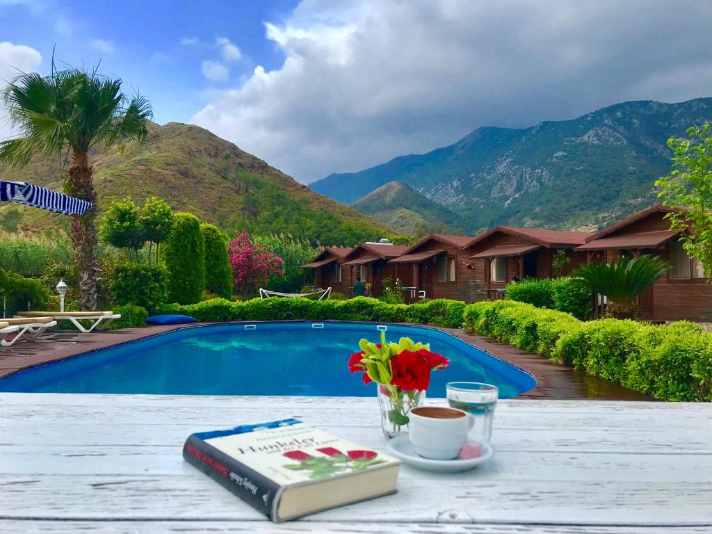 a table with a book and flowers on it next to a pool at Ada Adrasan Hotel in Adrasan