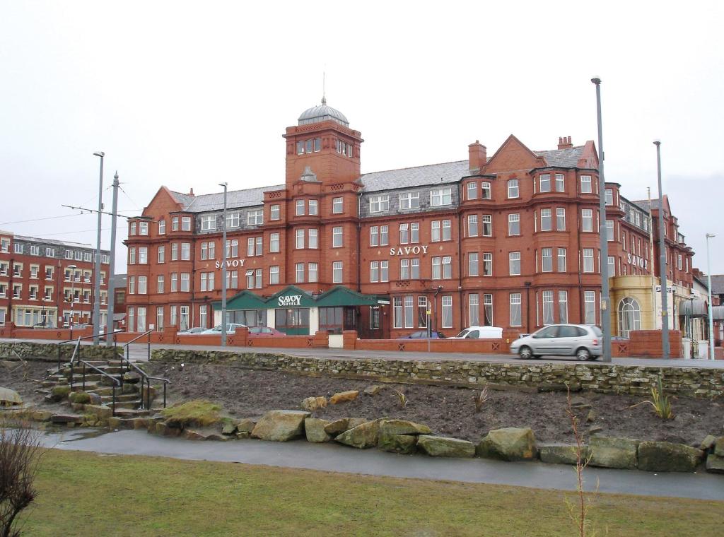 un grand bâtiment en briques rouges avec une voiture garée devant dans l'établissement The Savoy Hotel Adults Only, à Blackpool