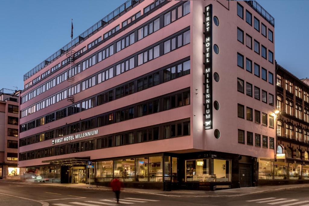 a person walking in front of a pink building at First Hotel Millennium in Oslo