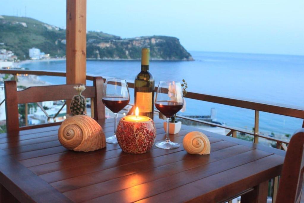 einem Holztisch mit Gläsern Wein und einer Kerze in der Unterkunft LIDO APARTMENTS in Himarë