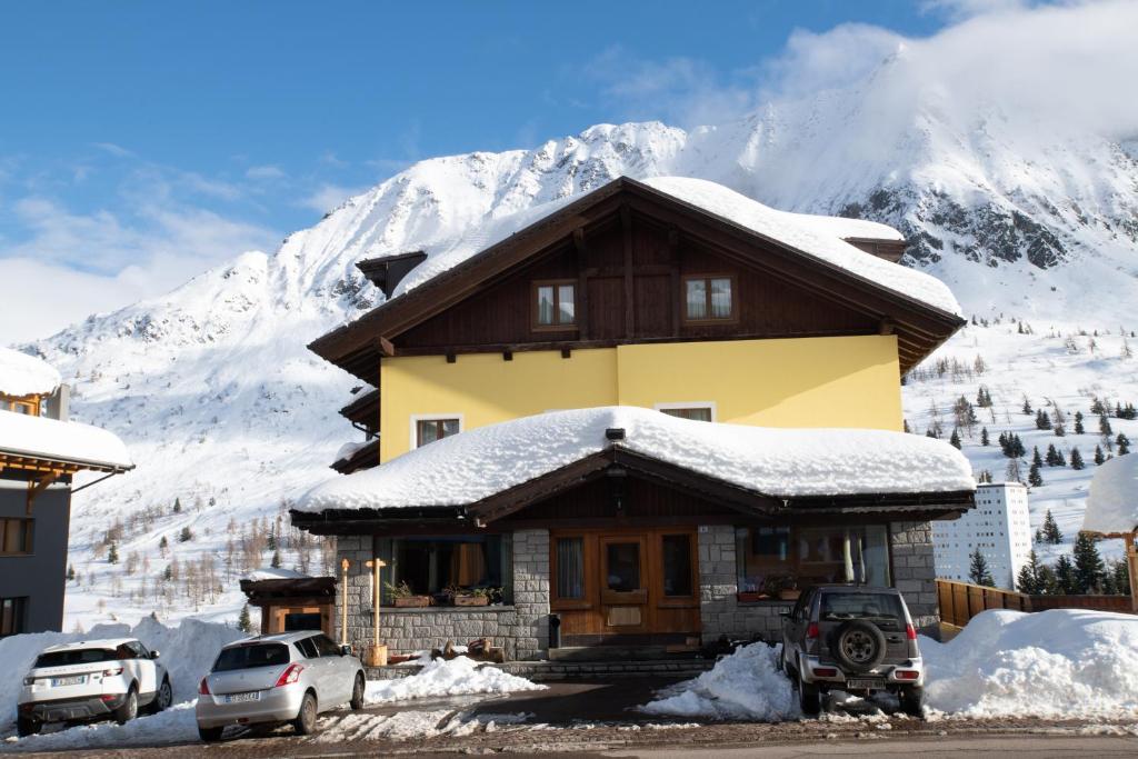 a house covered in snow with a mountain in the background at Hotel Angelo in Passo del Tonale