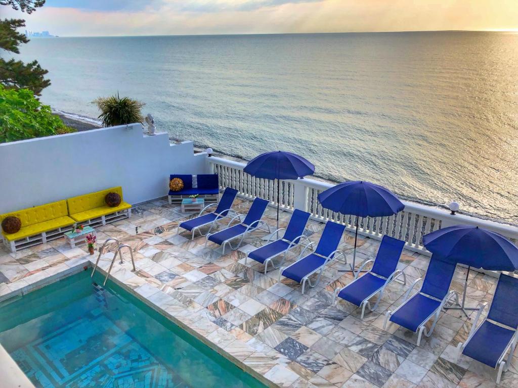 a pool with chairs and umbrellas next to the ocean at Hotel Tramonto in Chakvi