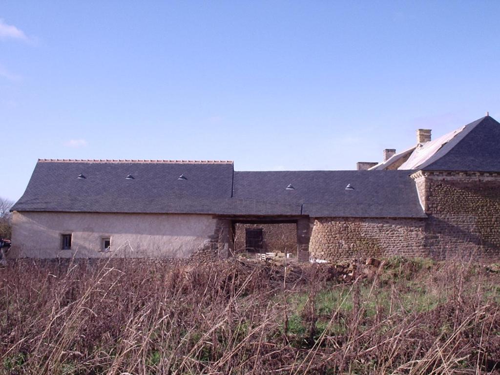 un vecchio edificio di mattoni con tetto nero su un campo di Gite et chambres de la porte du parc a Les Iffs