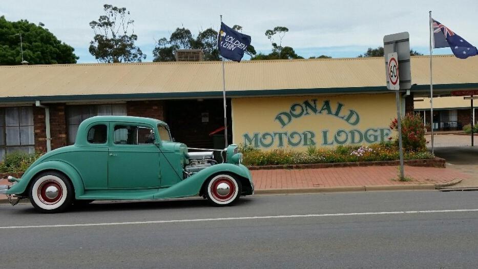 an old green car parked in front of a motor lodge at Donald Motor Lodge in Donald