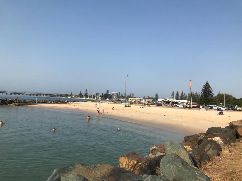 a beach with people in the water and a bridge at Reflections Tuncurry - Holiday Park in Tuncurry