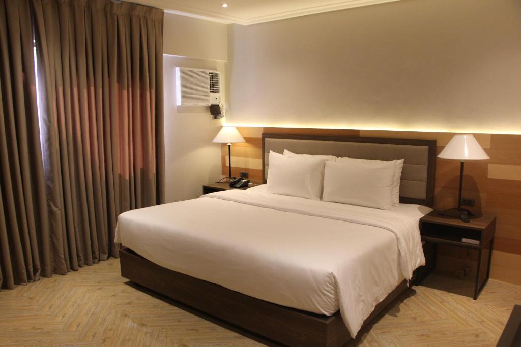 1 dormitorio con 1 cama grande con sábanas y almohadas blancas en Acacia Hotel Bacolod, en Bacolod