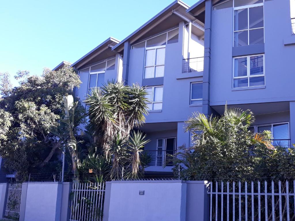 ein blaues Apartmenthaus mit einem Zaun und Bäumen in der Unterkunft Field's Rest: The Apartment in Port Elizabeth