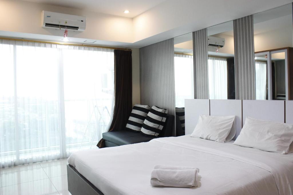 a bedroom with a large white bed and a chair at Bright Studio @ Tamansari La Grande Apartment By Travelio in Bandung