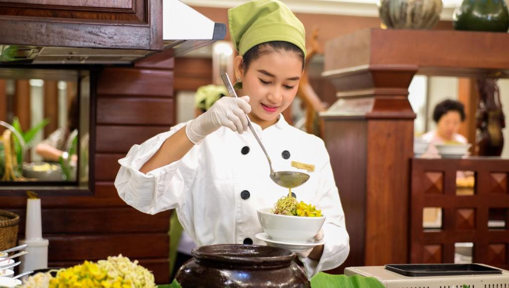 a woman in a kitchen stirring a bowl of food at Borei Angkor Resort & Spa in Siem Reap