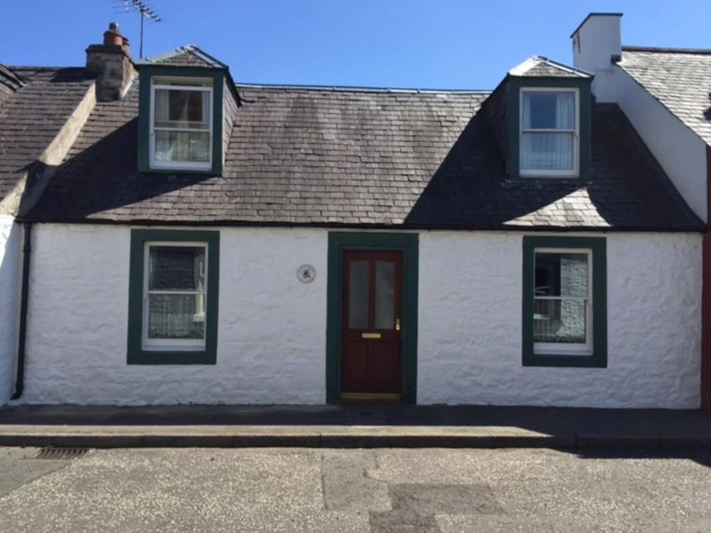 una casa blanca con una puerta roja en una calle en Lazydays Cottage, en Moffat