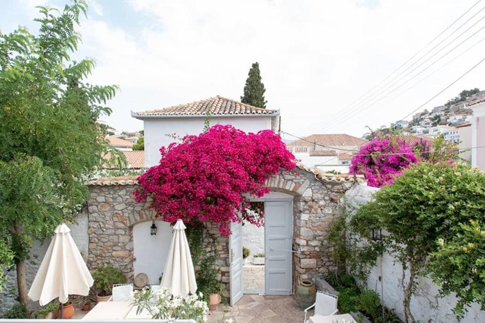 a white building with pink flowers and two umbrellas at Hotel Miranda in Hydra