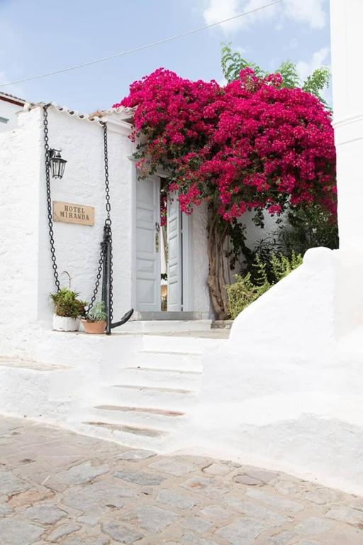 a white building with pink flowers on the side of it at Hotel Miranda in Hydra
