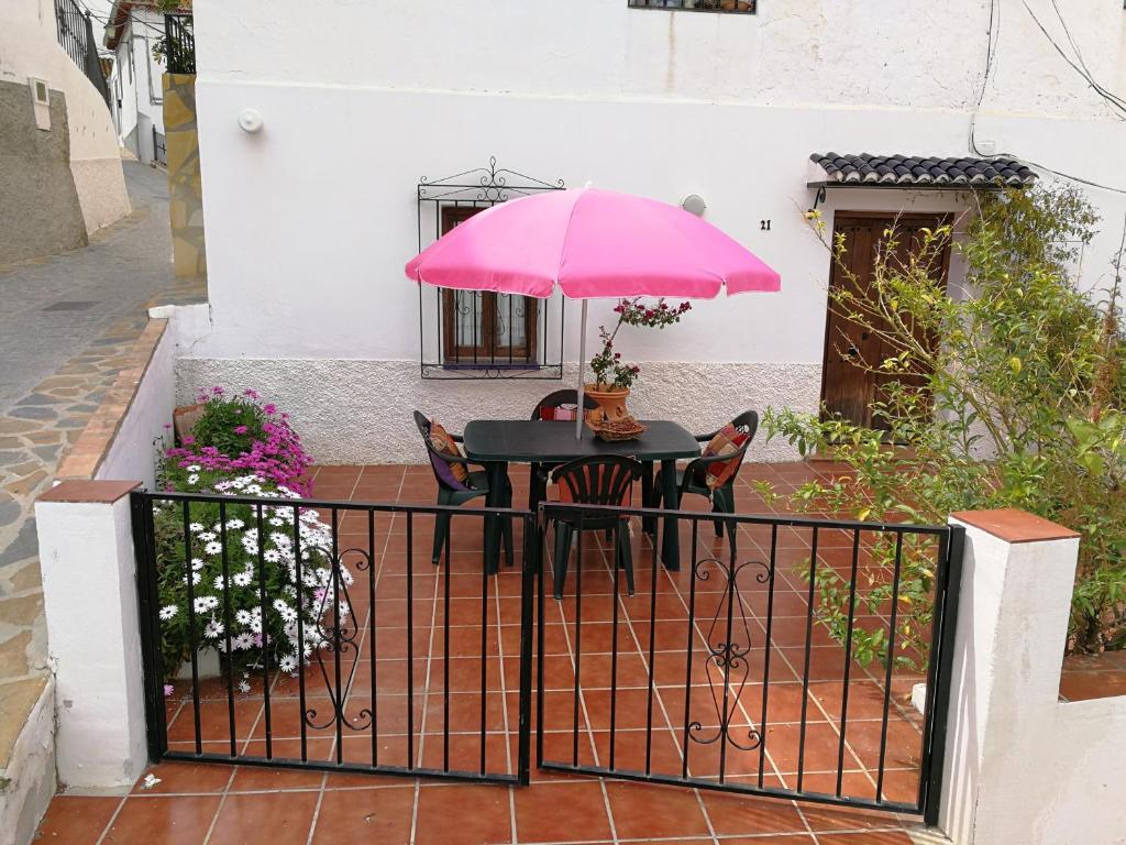 uma mesa com um guarda-chuva rosa numa cerca em Casa en pueblo de montes de Málaga a 15km de playa em Almáchar