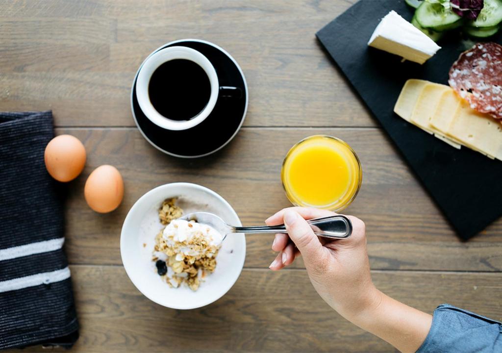 a person eating food with a bowl of cereal and a cup of coffee at Langley Hôtel Tignes 2100 in Tignes