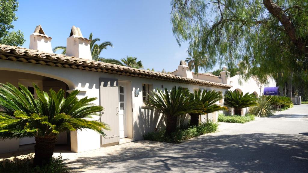 a white building with palm trees next to a driveway at Le Pre de la Mer in Saint-Tropez