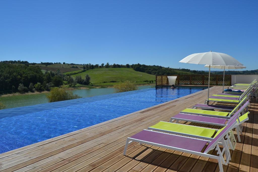 a row of lounge chairs and an umbrella on a swimming pool at Résidence L'Oustal Del Carlat in Carla-Bayle