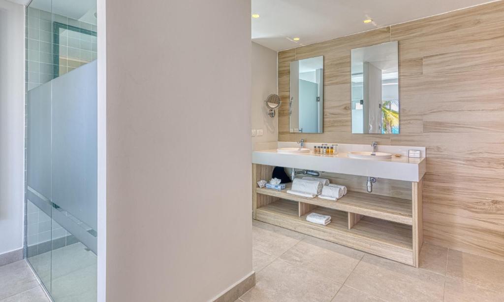 Modern bathroom with dual vanity sinks, wooden accents, mirrors, and walk-in shower.