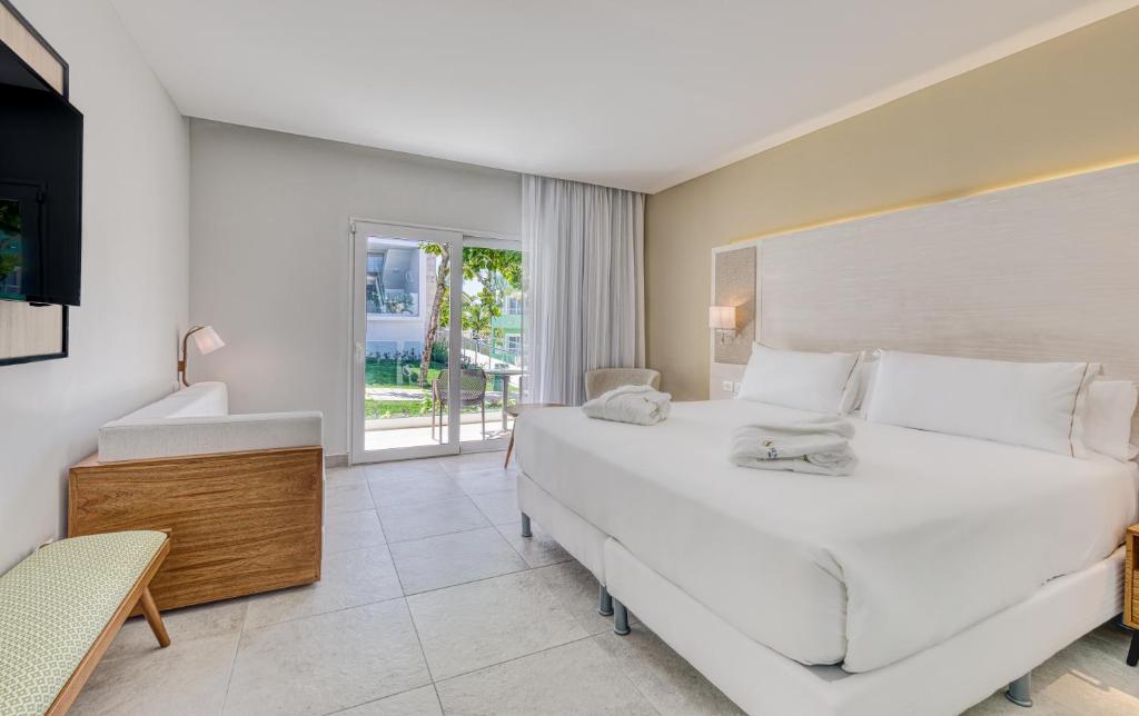 Hotel suite with king bed, wooden vanity, glass doors opening to balcony with ocean view.